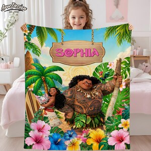 Puede incluir: Una manta personalizada con personajes de una popular pel&iacute;cula animada. La manta tiene un dise&ntilde;o vibrante con un tema tropical, que incluye palmeras, flores y el nombre "SOPHIA" en un letrero de madera. La manta es sostenida por una ni&ntilde;a.