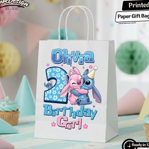 May include: White paper gift bag with the text "Olivia" and "2 Birthday Girl" in blue and pink. Features a cartoon illustration of Stitch and Angel hugging. Includes the text "Printed Paper Gift Bag".