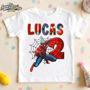 May include: White t-shirt featuring a colorful graphic of Spider-Man with the name "LUCAS" and the number "2". Spider-Man is wearing a party hat. The shirt is likely for a birthday celebration.