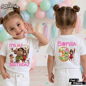 May include: White t-shirt with a colorful graphic featuring characters from the movie Moana, the text "IT'S MY BIRTHDAY" in pink, and the name "Sophia" on the back. The shirt is worn by a young child.