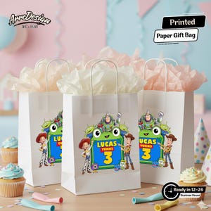 May include: Three white paper gift bags with white handles, each filled with light pink tissue paper. The front of each bag features a colorful graphic of Toy Story characters and a green sign with the text Lucas Turns 3.