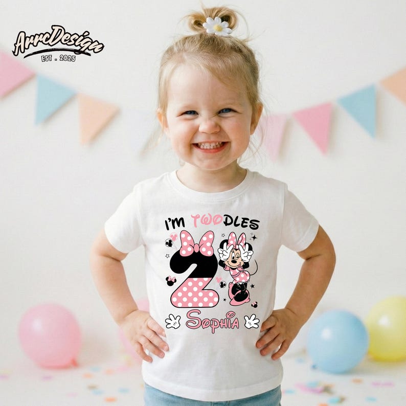 May include: White toddler t-shirt with a Minnie Mouse design. The design includes the text "I'm Twoodles" and "Sophia", along with a large number "2" in pink polka dots. The shirt is worn by a smiling child.