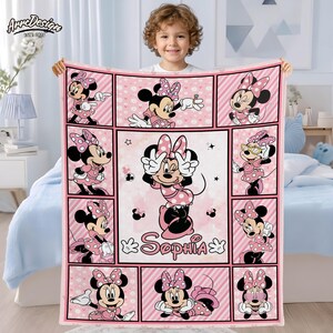 May include: Pink Minnie Mouse blanket with a grid pattern featuring Minnie Mouse in various poses. The blanket has a personalized name, "Sophia", and is held by a child. The blanket is made of soft material.