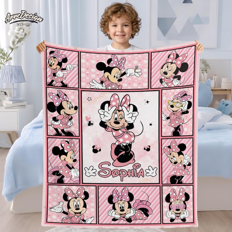 May include: Pink Minnie Mouse blanket with a grid pattern featuring Minnie Mouse in various poses. The blanket has a personalized name, "Sophia", and is held by a child. The blanket is made of soft material.