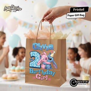 May include: A brown paper gift bag with the name "Olivia" and the number "2" printed on it. The bag features a cartoon illustration of two characters hugging, with the words "Birthday Girl" below. The bag is filled with tissue paper.