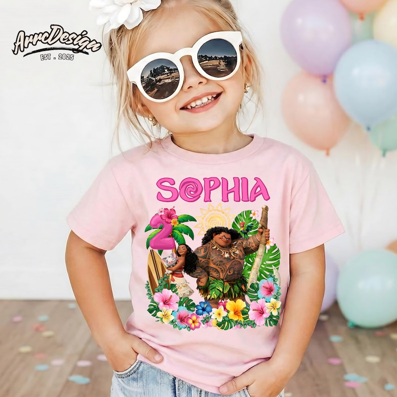 May include: A light pink t-shirt featuring the name "SOPHIA" in pink, with a tropical design including the number "2", flowers, and characters. The shirt is worn by a child wearing sunglasses.