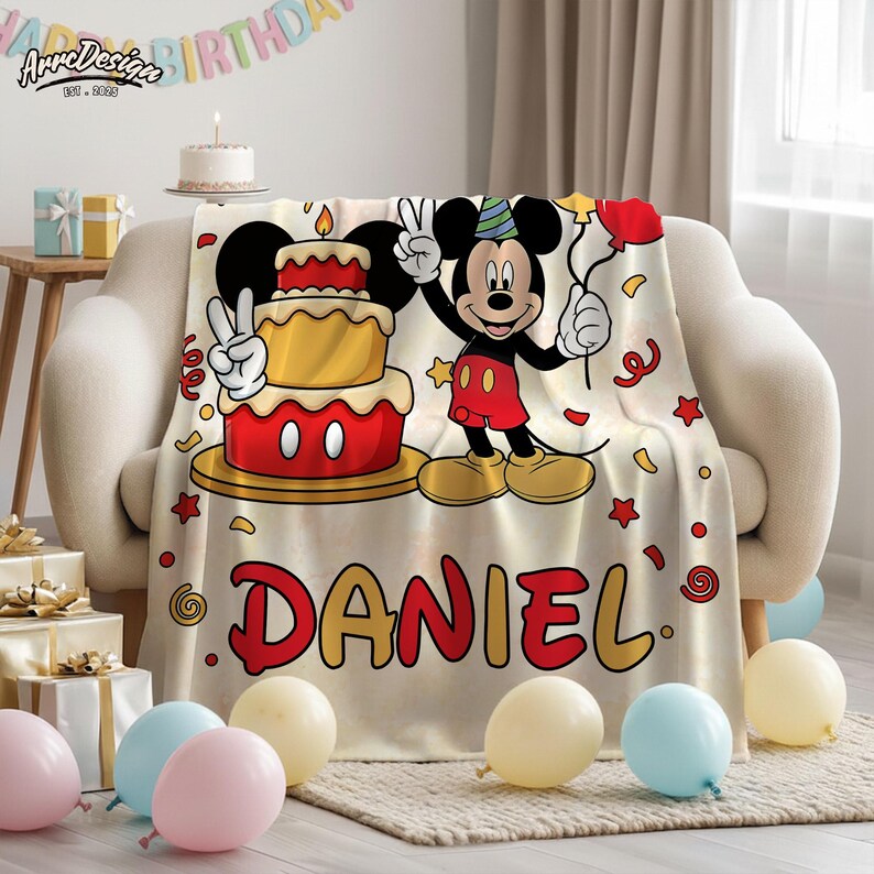 May include: A beige blanket featuring a cartoon Mickey Mouse design with a birthday cake and balloons. The blanket has the name "DANIEL" in red letters. The blanket is draped over a beige sofa, with balloons and gifts in the foreground.