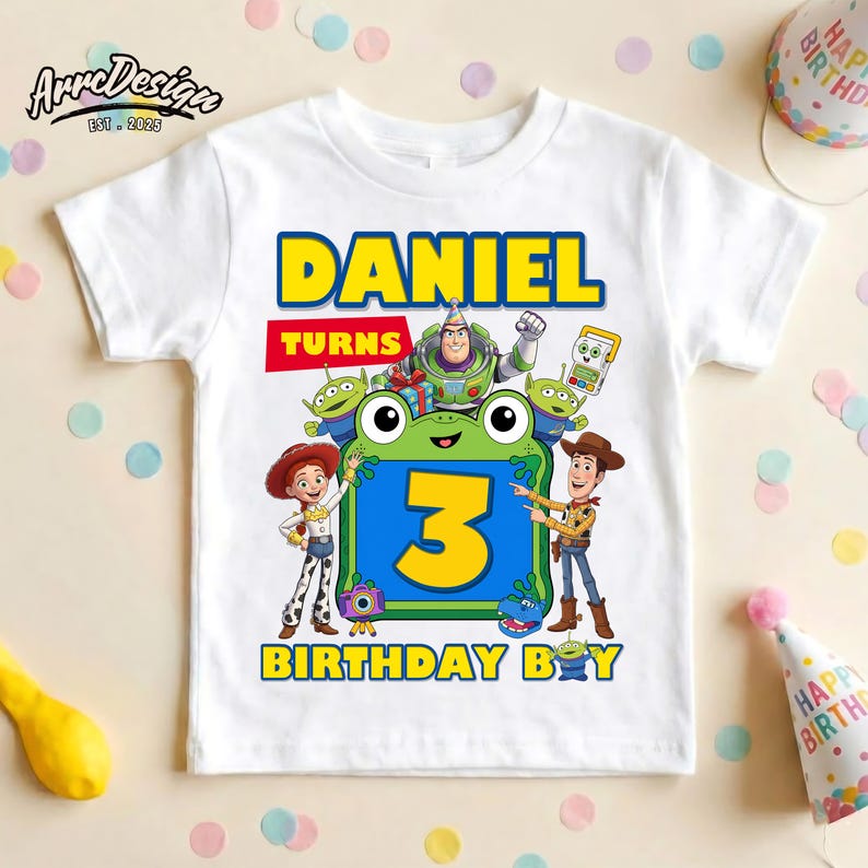 May include: A white short-sleeve t-shirt featuring a colorful graphic with the text DANIEL TURNS 3 BIRTHDAY BOY. The design includes cartoon characters Buzz Lightyear, Woody, Jessie, and green aliens surrounding a large yellow number 3.
