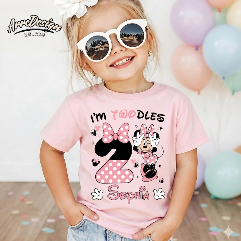 May include: A light pink t-shirt with the text "I'm Twoodles" and a Minnie Mouse design. The number "2" is in the center, with a polka dot pattern. The name "Sophia" is below the number.