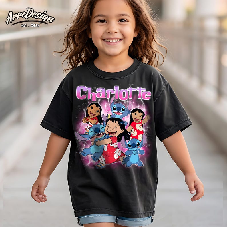 May include: A black short-sleeved t-shirt featuring a graphic print of the name Charlotte in pink letters above illustrations of Lilo and Stitch characters surrounded by a pink glowing aura and sparkles on a dark background.