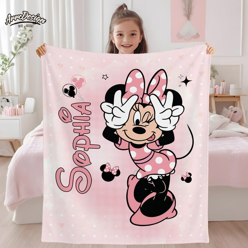 May include: Pink blanket featuring a Minnie Mouse design with polka dots and the name "Sophia" in pink script. The blanket has a light pink background with white polka dots and Minnie Mouse making a peace sign.