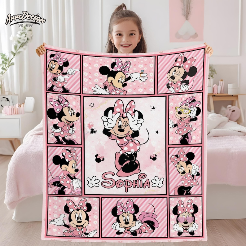 May include: Pink Minnie Mouse blanket featuring multiple images of Minnie in various poses. The blanket has a grid design with a central image of Minnie with the name "Sophia". The blanket is held up by a person.
