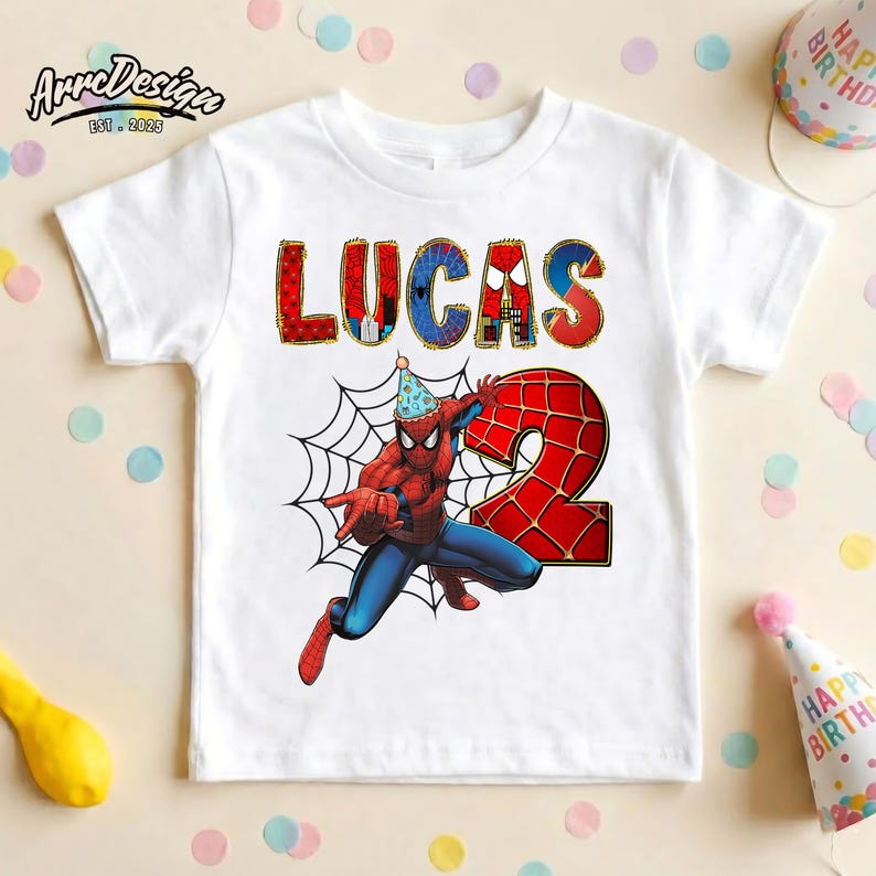May include: White t-shirt featuring a colorful graphic of Spider-Man with the name "LUCAS" and the number "2". Spider-Man is wearing a party hat. The shirt is likely for a birthday celebration.