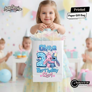 May include: A white paper gift bag featuring the name "Olivia", the number "2", and cartoon characters. The bag also has the text "Birthday Girl". The bag is held by a young girl at a birthday party.
