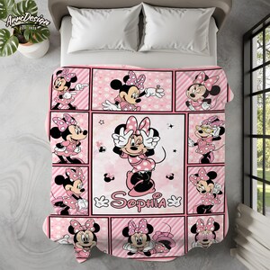 May include: A pink and white Minnie Mouse themed blanket featuring multiple images of Minnie Mouse in various poses. The blanket has a grid-like design with the name "Sophia" in cursive script. The blanket is on a bed with white pillows.
