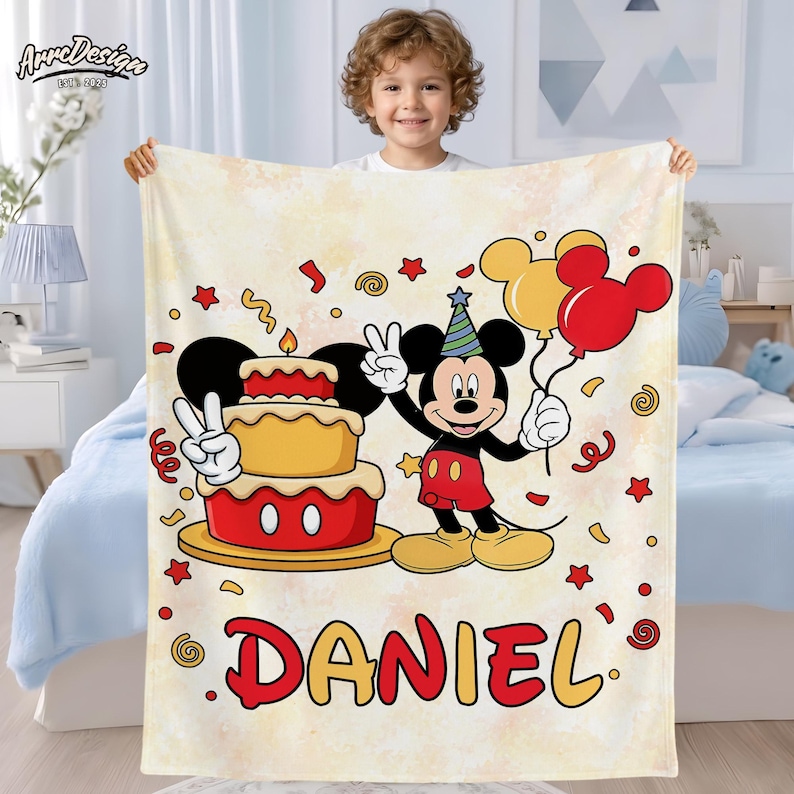 May include: A personalized blanket featuring Mickey Mouse holding balloons and a birthday cake. The blanket has a light yellow background with red and yellow accents, confetti, and the name "DANIEL" in red and yellow lettering. The blanket is held by a child.
