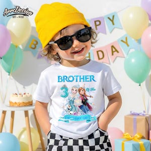May include: A white short-sleeve t-shirt featuring a graphic of two animated characters, a snowman, and the text BROTHER 3 OF THE BIRTHDAY GIRL. The design includes a large blue number three and icy blue accents on a white fabric background.