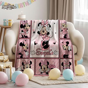 May include: A pink and white Minnie Mouse blanket with a grid pattern featuring Minnie Mouse in various poses. The blanket has the name "Sophia" printed on it. The background includes balloons and a birthday banner.