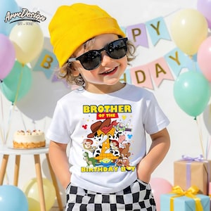 Puede incluir: Un ni&ntilde;o con una camiseta blanca con un gr&aacute;fico colorido de personajes de dibujos animados y el texto "Brother of the Birthday Boy". El ni&ntilde;o tambi&eacute;n lleva un gorro amarillo y gafas de sol. Globos y una pancarta de cumplea&ntilde;os en el fondo.