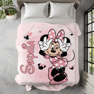 May include: A pink blanket with a Minnie Mouse design, featuring a polka dot bow and dress. The name "Sophia" is written in pink script. The blanket is decorated with stars and Minnie Mouse silhouettes.