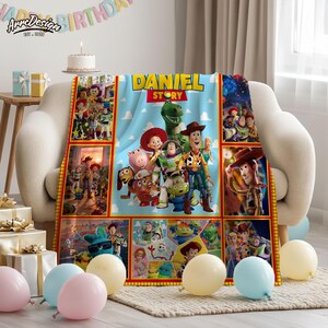 May include: A light blue blanket featuring characters from the movie Toy Story, with the name "DANIEL STORY" printed on it. The blanket is decorated with images of Woody, Buzz Lightyear, and other characters. The blanket is on a beige couch.