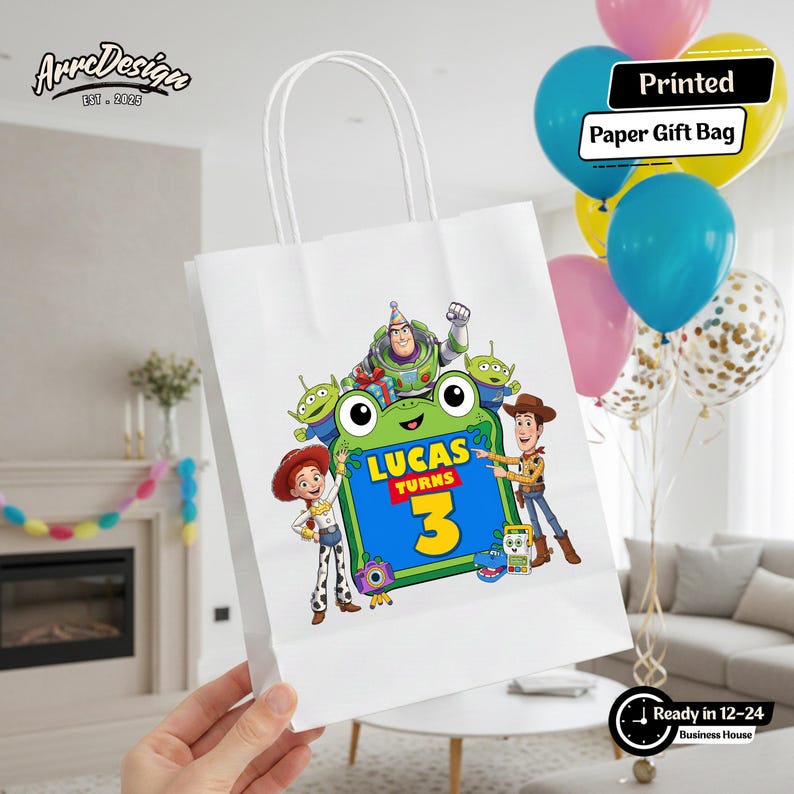 May include: A white paper gift bag featuring a colorful graphic of Toy Story characters including Buzz Lightyear, Woody, Jessie, and aliens surrounding a green frog-shaped frame with the text Lucas Turns 3 in blue and yellow lettering.