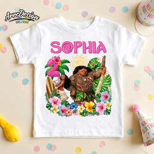 May include: White t-shirt featuring a colorful graphic of characters from the movie Moana, including Maui and Moana, with the name "Sophia" in pink letters and the number "2". The design is surrounded by tropical flowers and foliage.