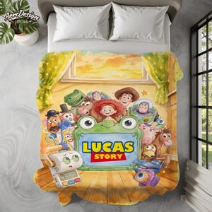 May include: A rectangular fleece blanket featuring a colorful illustration of various animated toy characters surrounding a central green frog-shaped frame. The text LUCAS STORY is printed in bold yellow and red letters inside the green frame.