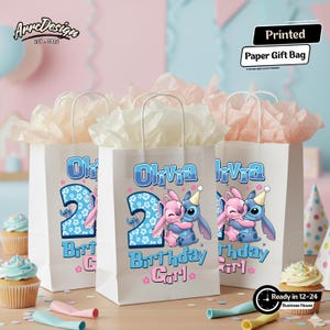 May include: Three white paper gift bags with handles, each featuring a design for a birthday girl. The bags have the name "Olivia", the number "2", and a cartoon character hugging another. The text "Birthday Girl" is also present.
