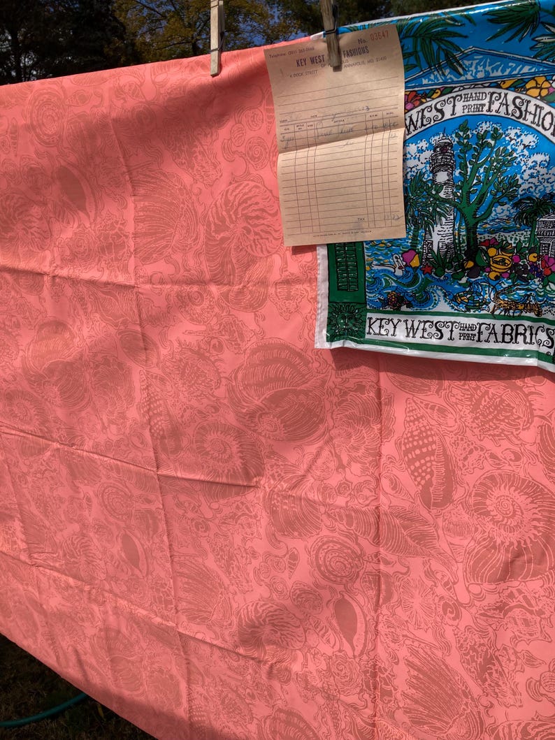 May include: Coral-colored fabric with a seashell pattern, hanging on a clothesline. A vintage receipt and a blue and green fabric with the text "WEST HAND PRINT FASHIONS" are also visible.