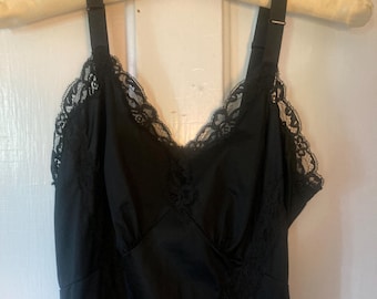 May include: A black slip dress with delicate lace trim along the neckline and straps. The dress is hanging on a vintage satin hanger. The fabric appears to be a smooth, silky material.