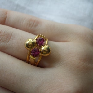 Könnte beinhalten: Ein goldener Ring mit drei runden, erhabenen Goldfassungen. Jede Fassung hat einen kleinen, runden, rosafarbenen Edelstein.