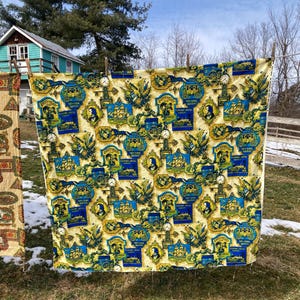 Könnte beinhalten: Ein Vintage-Stoff mit einem sich wiederholenden Muster aus blauen und gelben Illustrationen von Schiffen, Kutschen, Porträts und Uhren. Der Stoff hängt draußen an einer Wäscheleine. Der Hintergrund umfasst ein kleines Haus und Bäume.