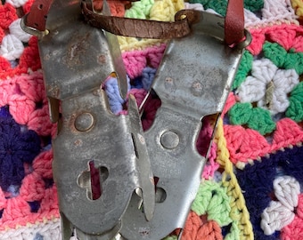 May include: A pair of vintage metal ice skates with leather straps, showing signs of wear. The skates are silver-toned with a cross-shaped design on the front. The background is a colourful, crocheted blanket.