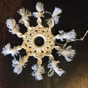 May include: A white crocheted snowflake with a hole in the center and white fringe around the edges.