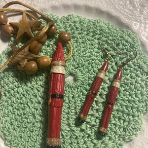 May include: A set of Christmas-themed earrings and a pendant featuring a red and white Santa Claus figure. The earrings and pendant are made of wood and painted with red, white, and black paint.