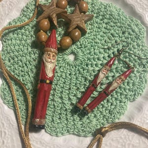May include: A set of wooden Christmas ornaments featuring a Santa Claus pendant, a pair of Santa Claus earrings, and a necklace with wooden beads and stars.