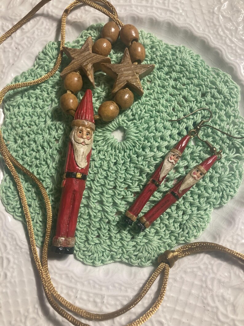 May include: A set of wooden Christmas ornaments featuring a Santa Claus pendant, a pair of Santa Claus earrings, and a necklace with wooden beads and stars.