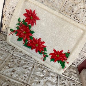 May include: Rectangular serving tray with a cream-colored background and a poinsettia design. The poinsettias are red with green leaves and red berries. The tray has a slightly textured surface.