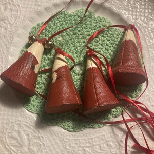 May include: Four red and white Christmas tree ornaments with gold bells and red ribbon.