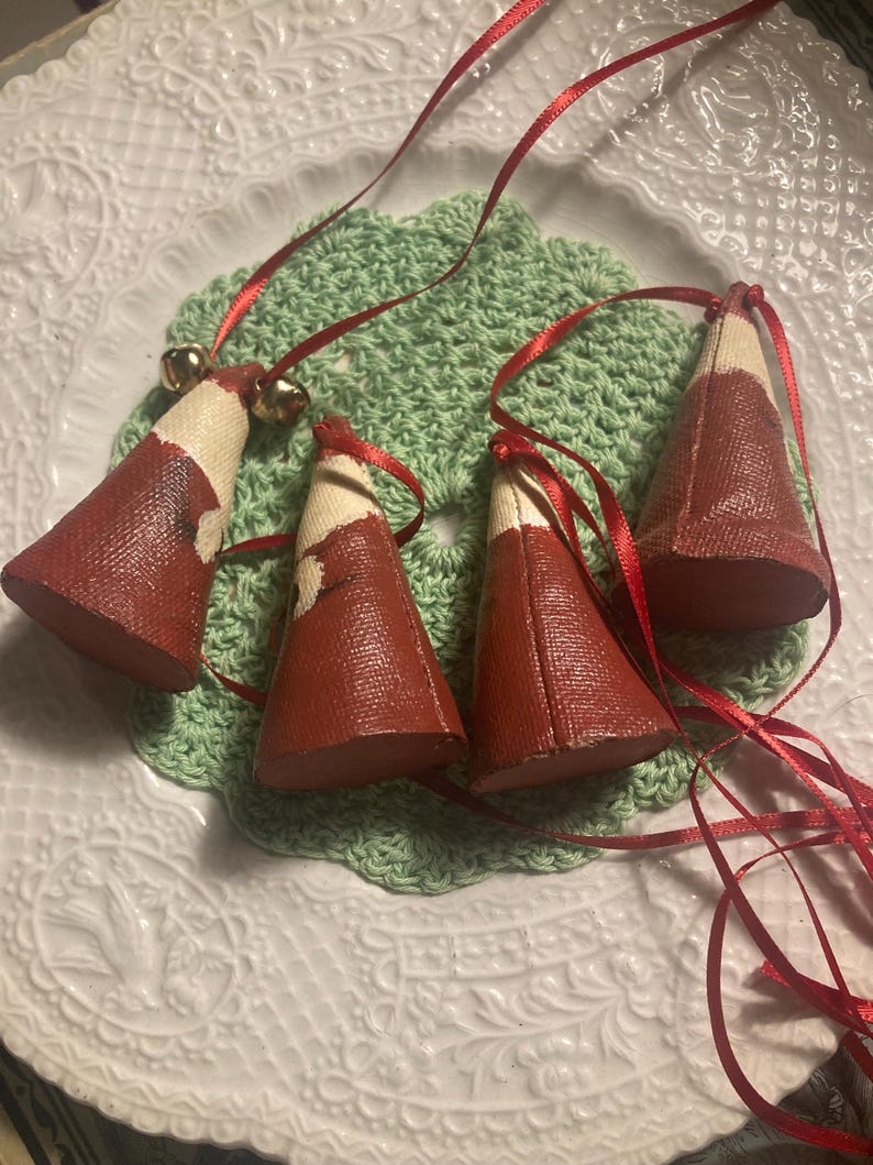 May include: Four red and white Christmas tree ornaments with gold bells and red ribbon.