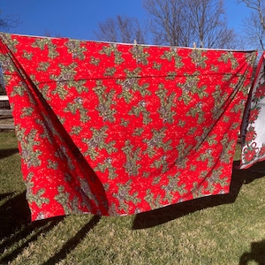May include: Red tablecloth with a green and white snowflake pattern. The tablecloth is hanging on a clothesline outdoors.