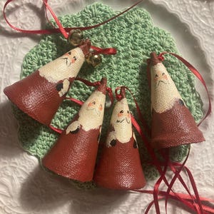 May include: Four small red felt Christmas ornaments with painted Santa faces and white trim. Each ornament has a gold bell attached to a red ribbon.