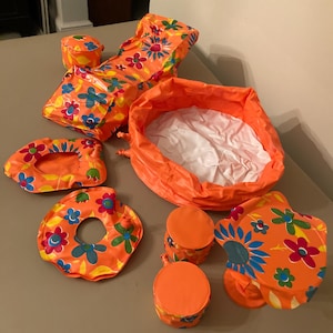 May include: A set of inflatable pool toys in orange with a floral pattern. The set includes a small pool, two chairs, two stools, and two inner tubes.