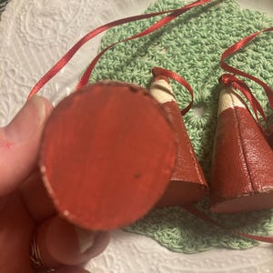 May include: Two red fabric cone-shaped ornaments with white trim and red ribbon ties. The ornaments are on a green crocheted surface.