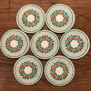 Pode incluir: Conjunto de sete  copos de papel branco, verde e vermelho com um design de coroa. Cada copo apresenta uma coroa verde com bagas vermelhas e bolinhas brancas.