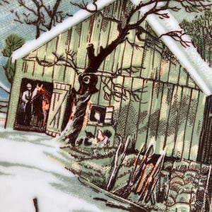 May include: A vintage plate featuring a winter scene with a barn, a horse, and a rider. The barn is painted in shades of green and brown, with a snowy roof and a tree in front. The plate has a detailed, hand-painted aesthetic.