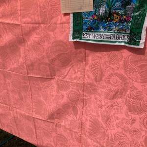 May include: Coral-colored fabric with a seashell pattern. A green and white bag with the text "Key West Fabrics" and a lighthouse graphic is visible. A paper receipt is also present.