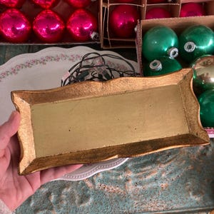 May include: A rectangular gold-toned tray with a smooth, flat center and textured, flared edges. The tray features a metallic finish and a slightly curved, decorative border design, providing a structured surface for holding small items.