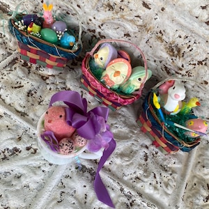 May include: Four decorative Easter baskets filled with colorful eggs, chicks, and bunnies. The baskets are made of woven materials and decorated with ribbons and flowers. The baskets are in various colors, including pink, purple, blue, and green.